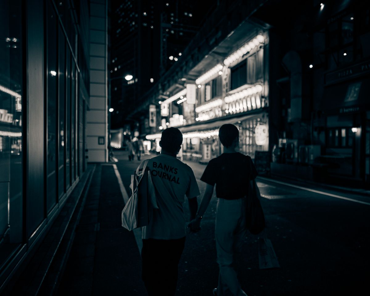 A couple holding hands and walking together along a bright city street in the evening