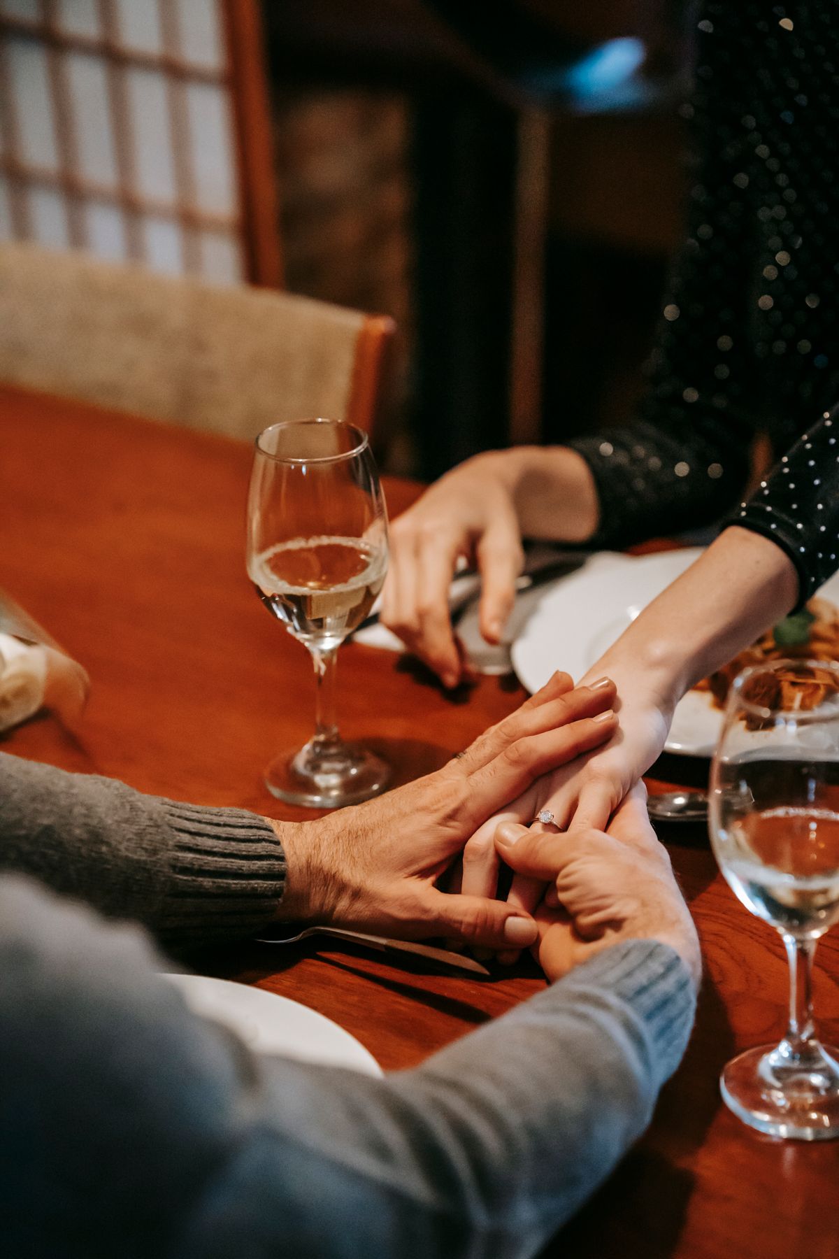 A couple holding hands over a candlelit dinner with wine at a cozy restaurant table