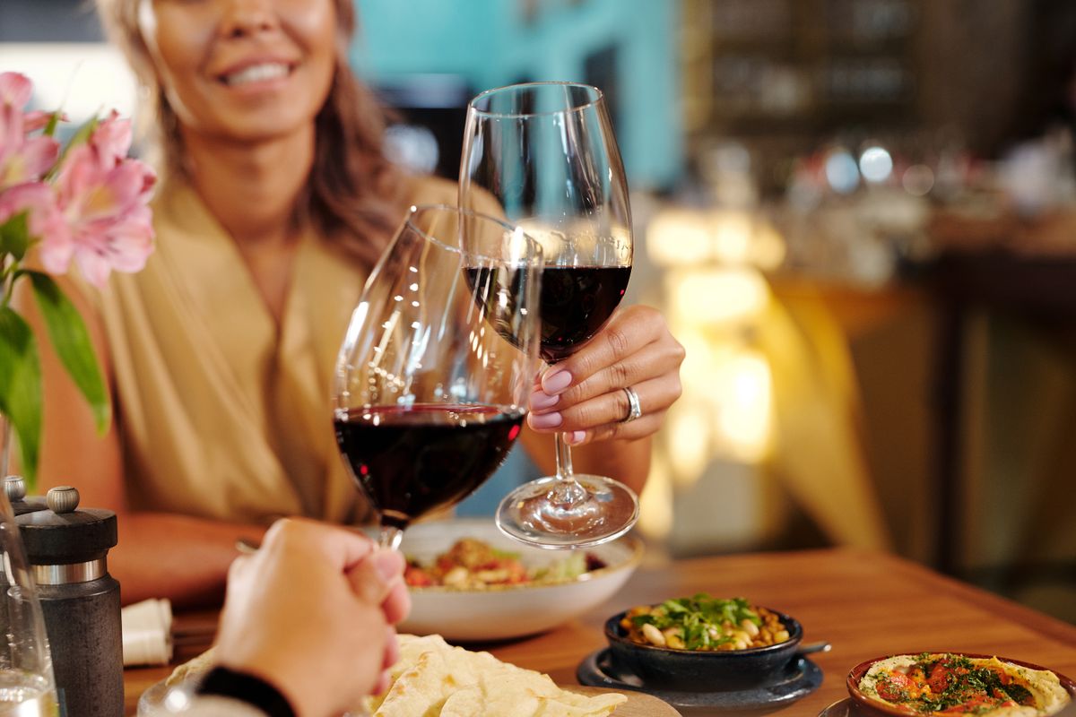 A couple toasts with glasses of red wine across a candlelit restaurant table