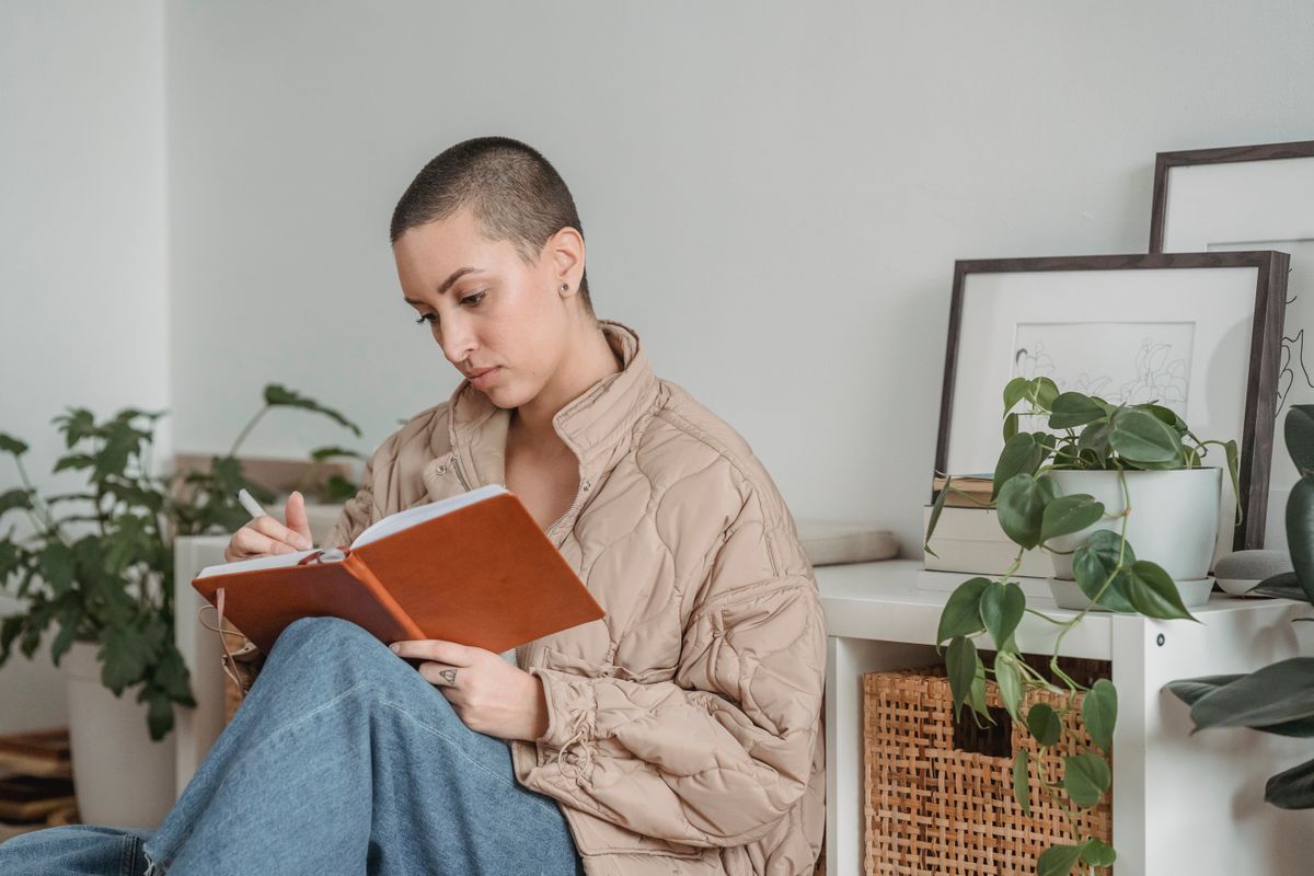 A woman sits at home writing thoughtfully in a journal beside a cup of coffee