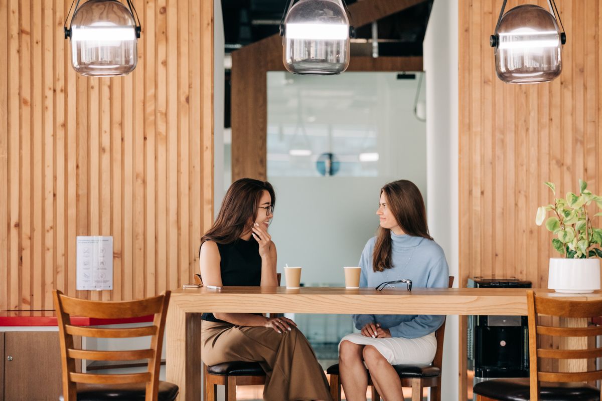 Two friends lean in and talk warmly over coffee at a bright cafe table