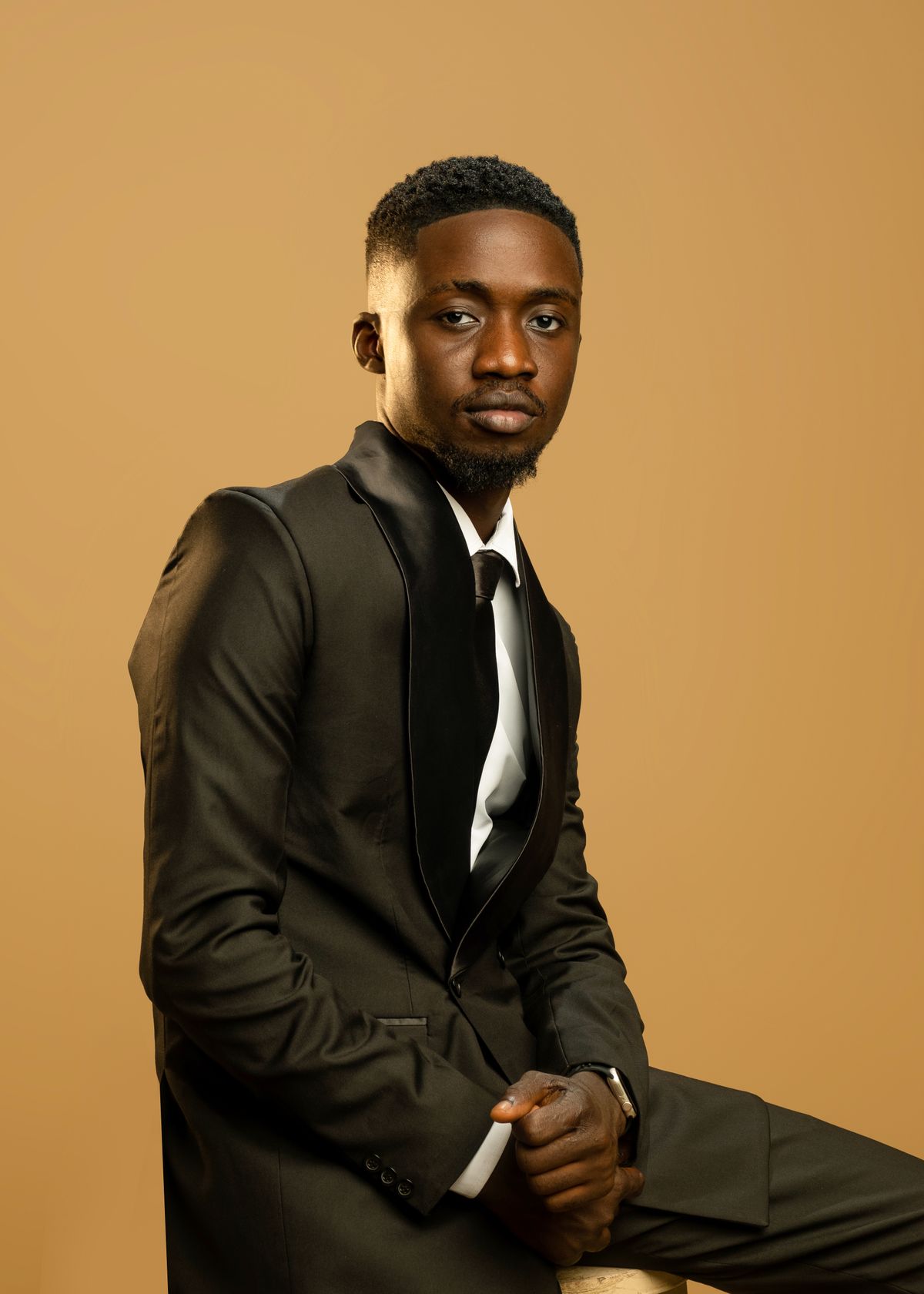 A confident man in a tailored suit smiles for a portrait against a warm backdrop