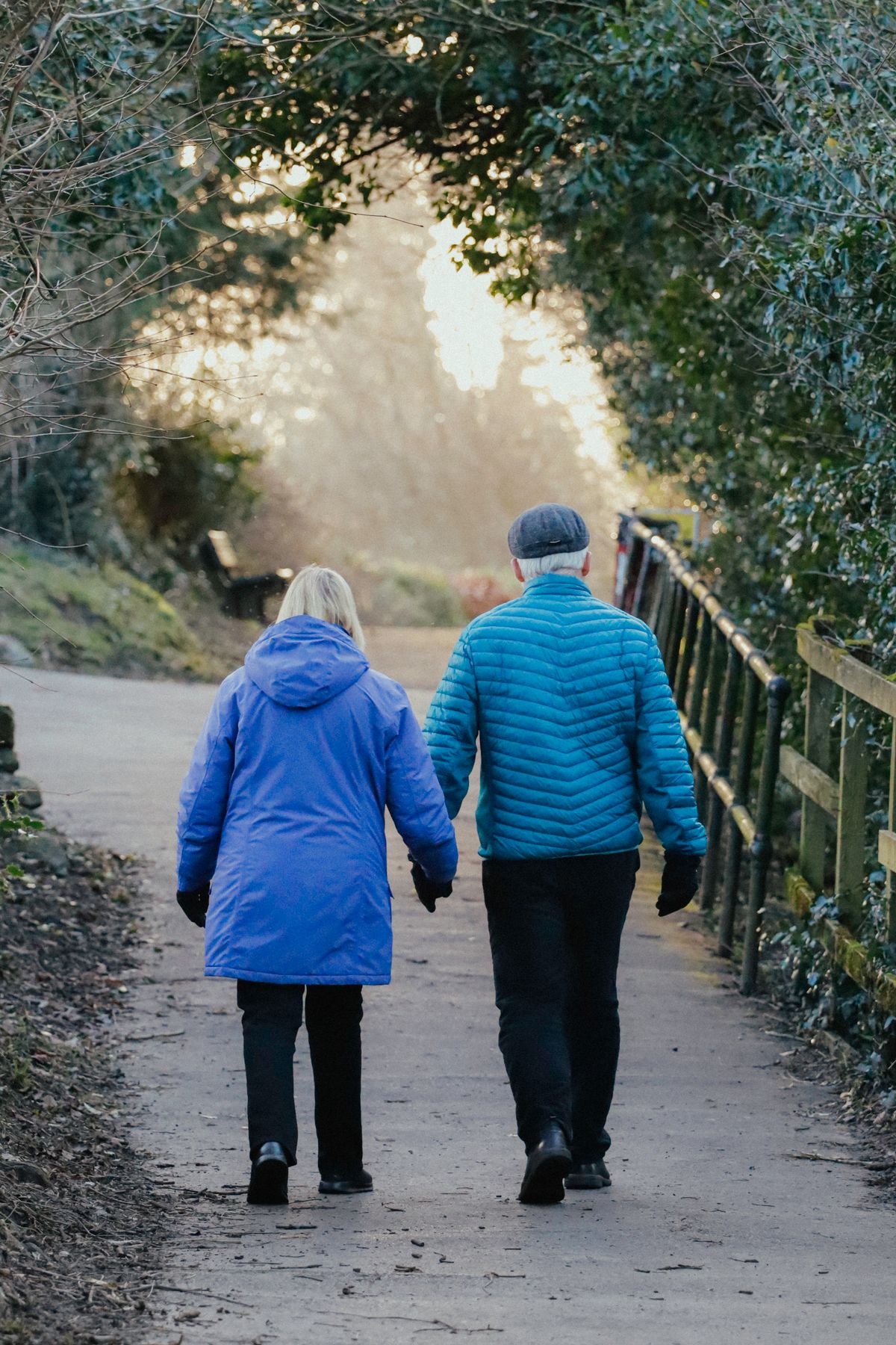 An older couple walking together along a tree-lined park path on a mild day