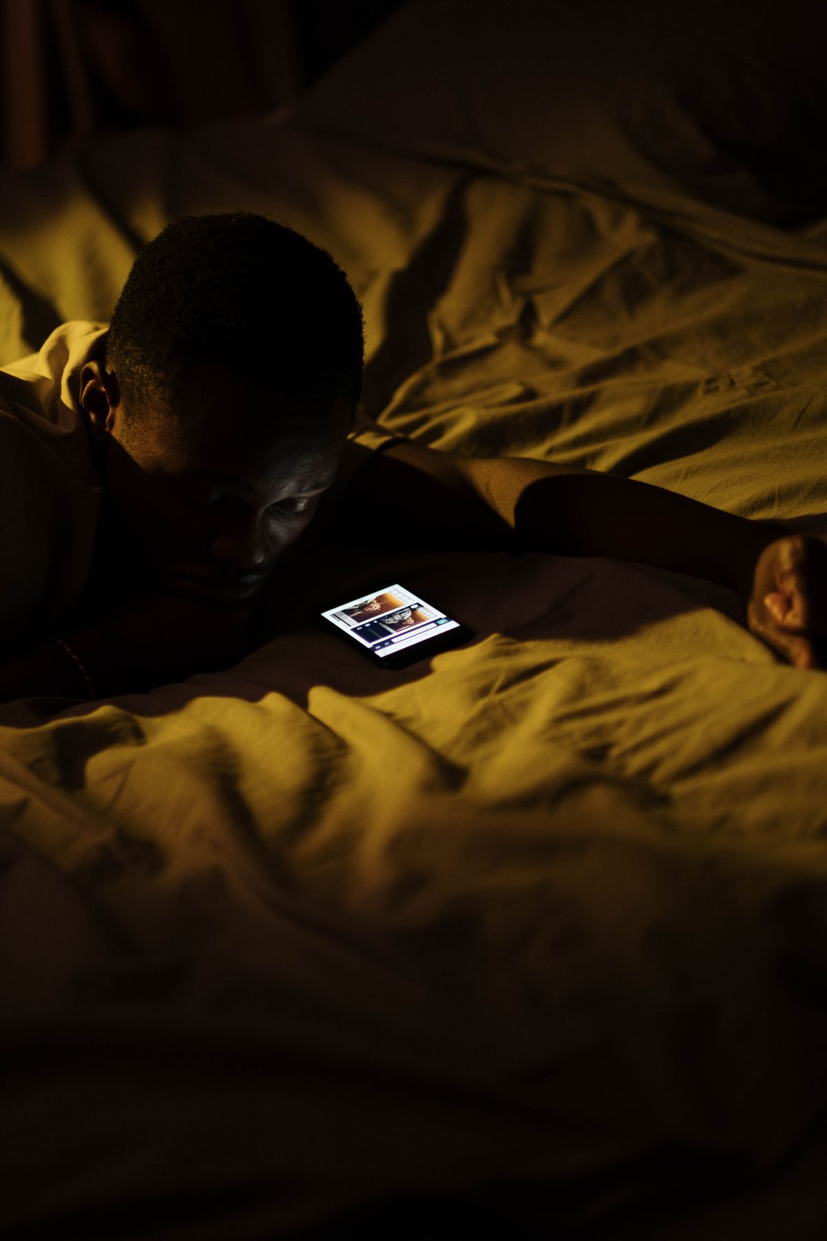 A man lies in bed at night, his face lit by his phone screen, scrolling instead of sleeping