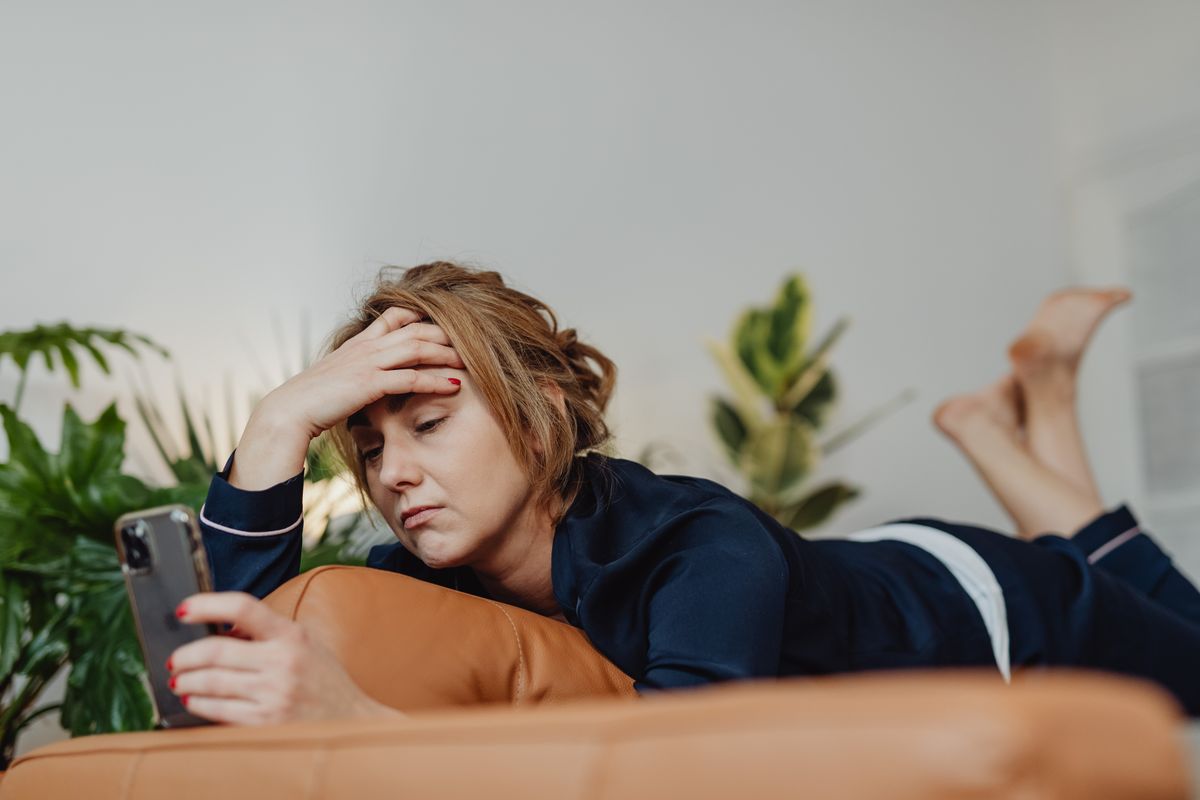 A woman on her couch looks stressed and frustrated at her cellphone screen