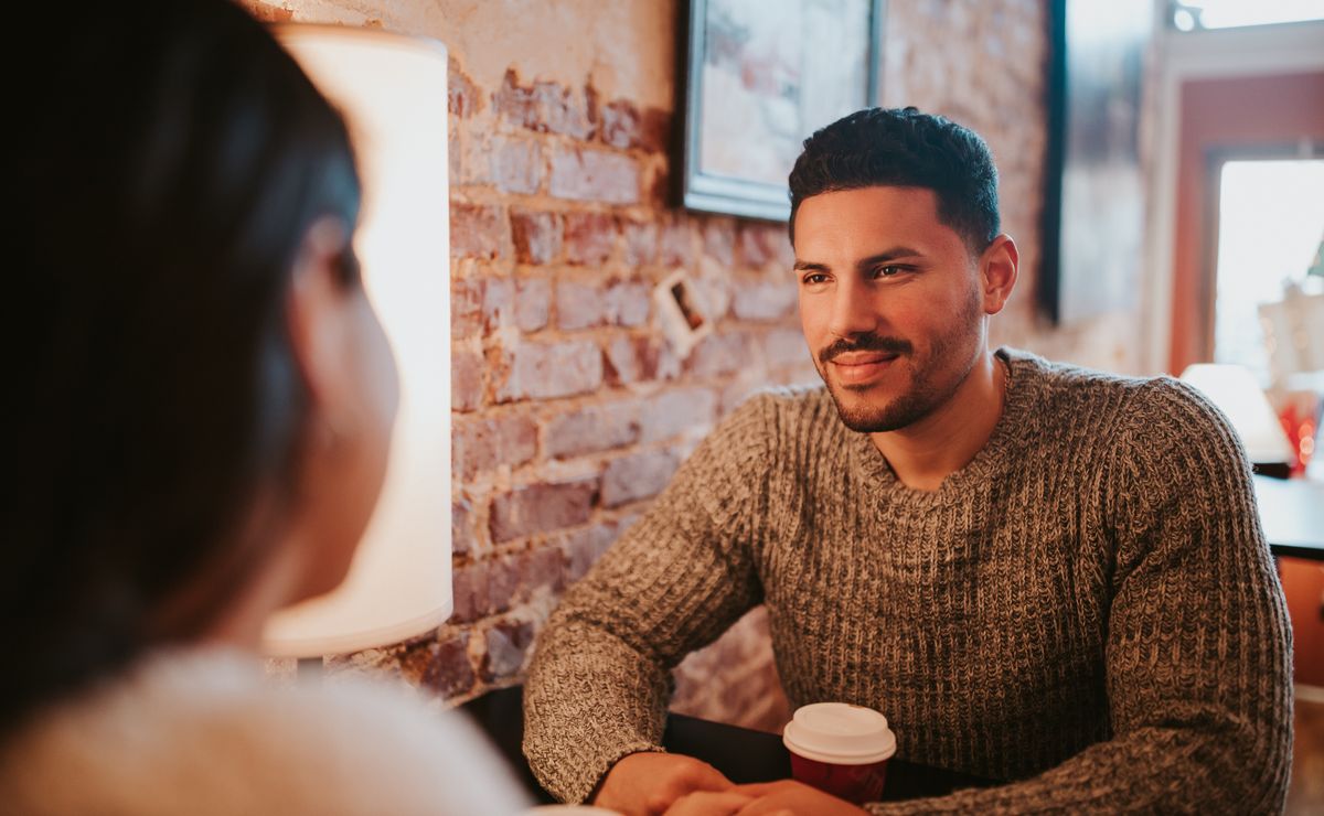 A couple shares warm, affectionate smiles across a cafe table on a real in-person date