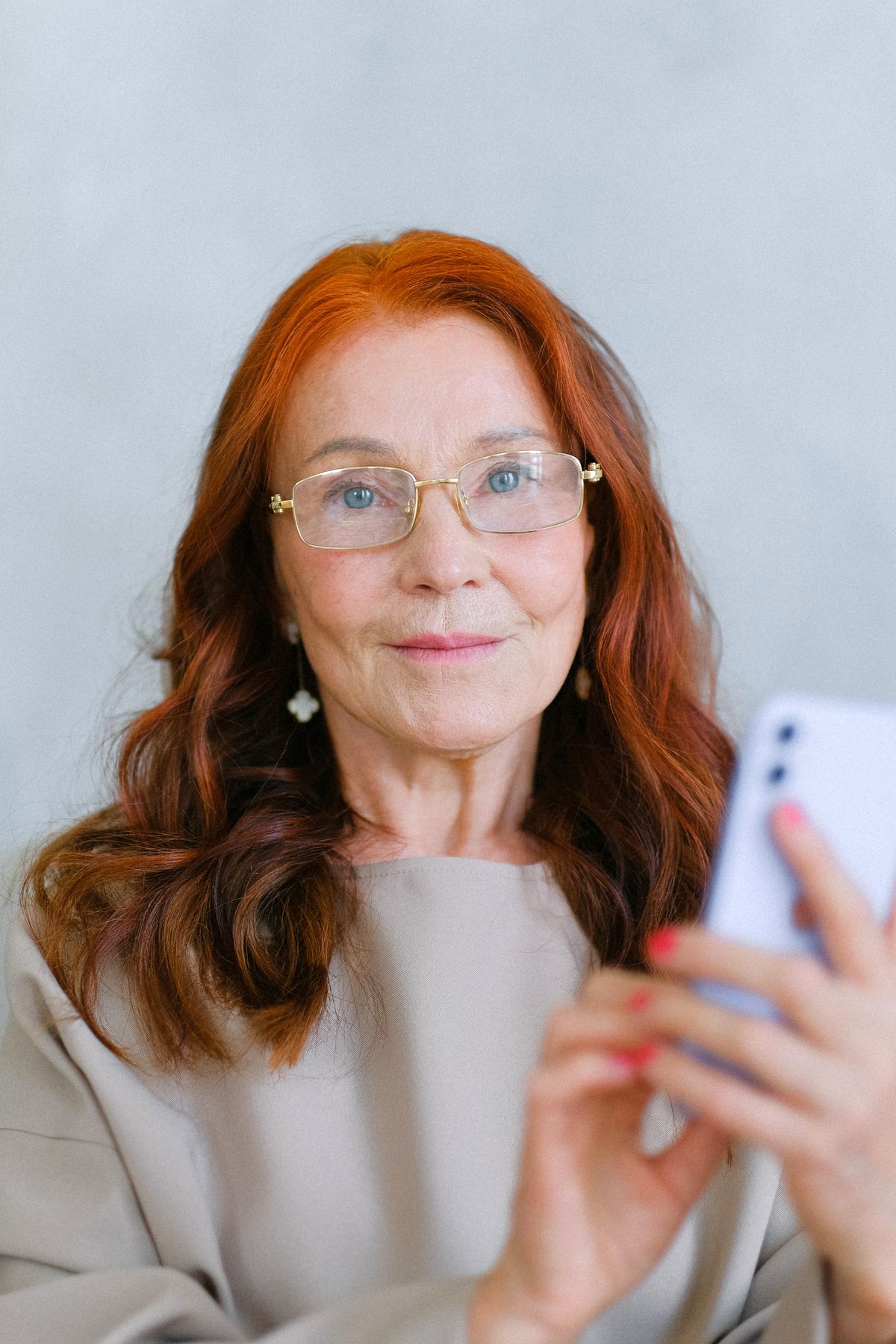 A mature woman in glasses scrolling on her smartphone, reflecting the effort of online dating after 50