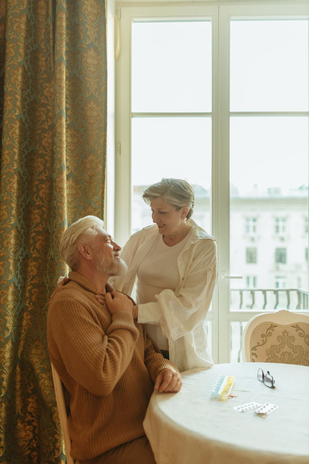 An older couple smile warmly at each other by a window, staying open to new love in later life