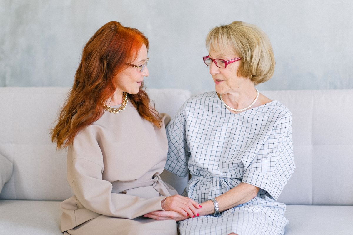An older woman holds hands and talks warmly with a trusted confidante, evoking matchmaker guidance and support