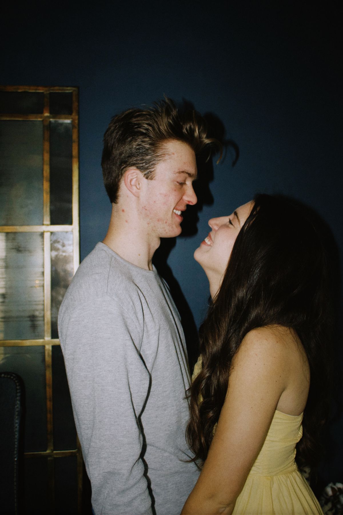A couple laughs and gazes at each other in a softly lit room, sharing a joyful, hopeful moment