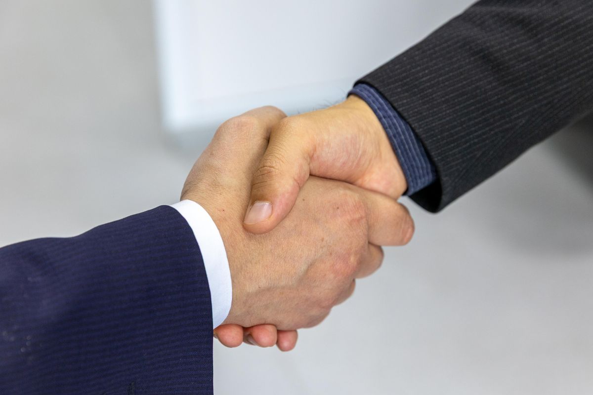 Two professionals in suits shake hands, symbolizing a trusted personal introduction and partnership