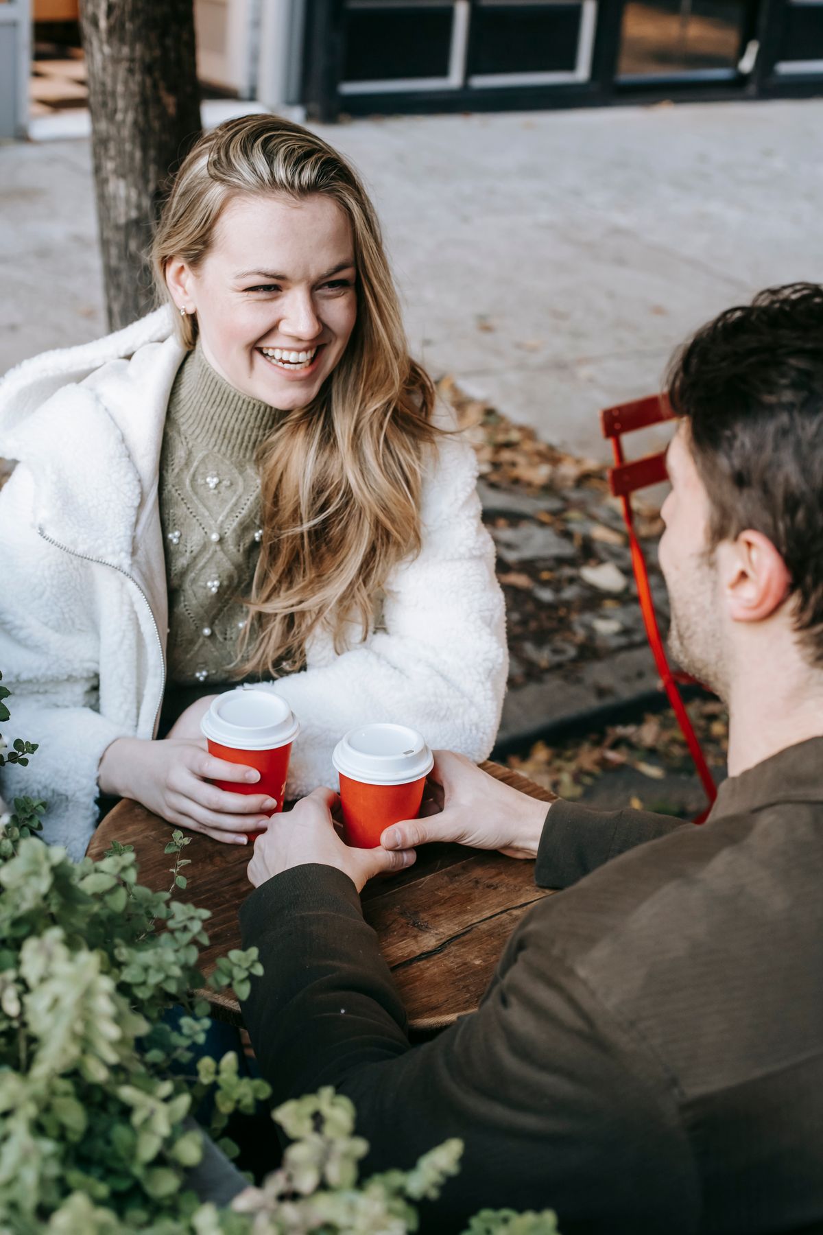 A couple smiling at each other over coffee on a sunny cafe terrace
